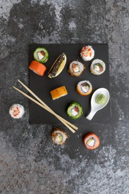 Suşi gri beton arka planda. Gökkuşağı suşi rulosu, uramaki, hosomaki ve nigiri.