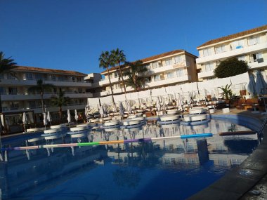 İspanya 'nın Magaluf kentindeki BH Mallorca Oteli' nde yuvarlak yataklı ve güneşli havuz. 30 Eylül 2019 'da sabah erken saatlerde çekilmiş. İnsan yok. Parlak mavi gökyüzü ve modern apartmanlar.