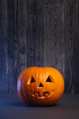 Gülümseyen bir yüzle oyulmuş balkabağı, koyu ahşap bir zemin üzerine aydınlatılmış, Cadılar Bayramı ve sonbahar kutlamaları için şenlikli bir ortam yaratıyor.