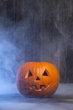 Karanlık ortamda parlayan balkabağı-fener, sis ile çevrili, oyulmuş özellikler ve canlı turuncu renk, neşeli bir Cadılar Bayramı atmosferi yaratıyor