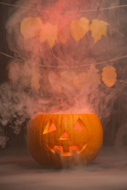 Renkli sonbahar yapraklarıyla çevrili, oyma şekilli, parlak bir fener, Cadılar Bayramı kutlamaları için ürkütücü bir ortam yaratıyor.