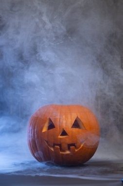 Gülümseyen bir yüzle oyulmuş balkabağı, sisle kaplanmış, ürkütücü bir atmosferi çağrıştırıyor, Cadılar Bayramı ve sonbahar kutlamaları için mükemmel.