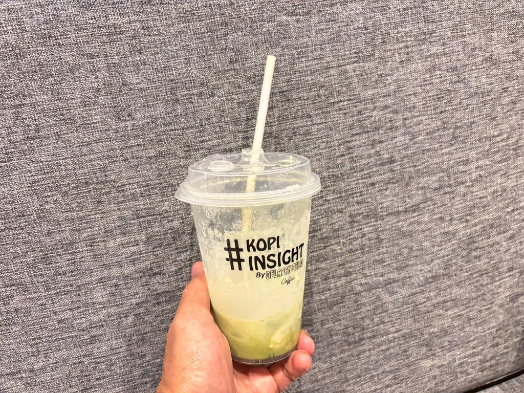 Bandung, Indonesia - September 21, 2025 : Hand holding iced matcha latte coffee cup