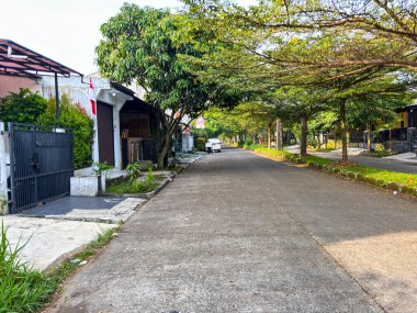 Bandung, Endonezya - 26 Eylül 2025: Yeşil ağaçlarla kaplı güneşli konut yolu