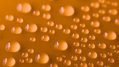 Turuncu yüzeydeki su damlacıkları makroda yakalandı. Tasarım, geçmiş, ambalaj ve güzellik için uygun. Moda, içecek ve sağlık reklamlarına uygulanabilir.