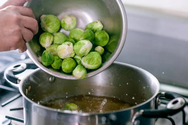 Bir kadının elleri, sıcak su dolu bir tencerede pişirmek için Brüksel lahanası koyuyor.. 