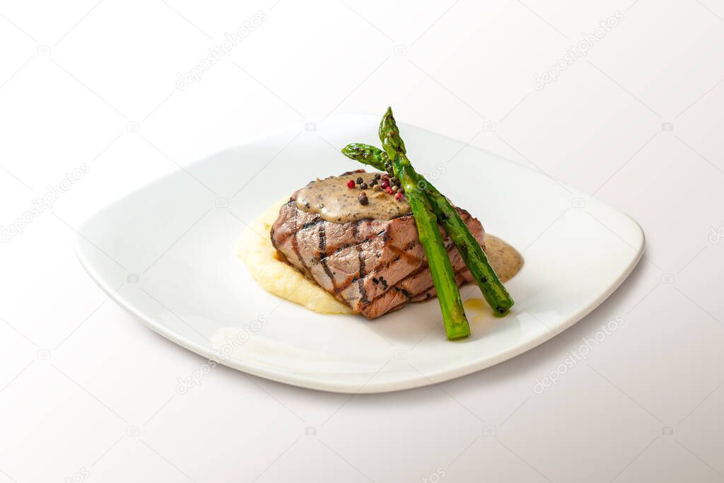 Filet mignon over mashed potatoes with asparagus on a white plate isolated on white.