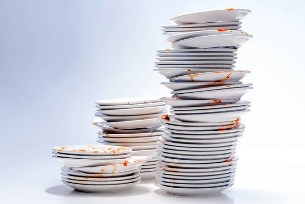 Beyaz arka planda yığılmış bir sürü kirli tabak.