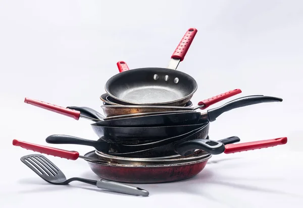 Beyaz arka planda aşınan tavalar ve mutfak aletleri.