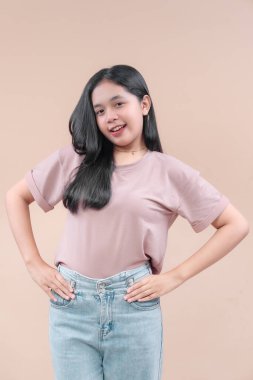 Gündelik modern moda içinde genç bir Asyalı kadın, elleri belinde, Pastel bir tişört ve kot pantolon giyerken özgüvenle duruyor..