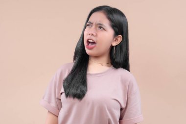 Gündelik modern kıyafetli genç bir Asyalı kadın, basit bir nötr geçmişe karşı duygusal tepki verirken pastel bir tişört giyip sorgulama bakışlarıyla şaşkınlığını dile getiriyor..