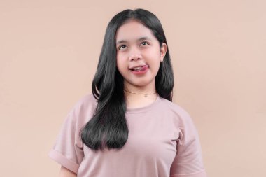 Asyalı modern kıyafetler giymiş, neşeli ifadeli, gözlerini deviren, dilini dışarı çıkaran eğlenceli, kendine güvenen ve genç bir kişilik sergileyen bir kadın..