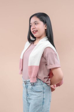 Modern tarzda giyinmiş Asyalı bir kadın. Pastel gömlek ve açık renk kot pantolon giyiyor. Örgü kazaklı..