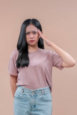 Modern kıyafetli Asyalı genç bir kadın şakağına ciddi bir yüzle dokunuyor. Stres ve rahatsızlığını ifade ediyor. Baş ağrısını ya da baskıyı simgeliyor..