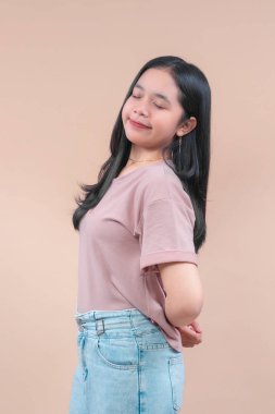 Uzun siyah saçlı, pastel bir tişört ve açık renk kot pantolon giyen, gözleri kapalı gülümseyen, rahat ve neşeli modern yaşam tarzını ifade eden Asyalı bir kadın..