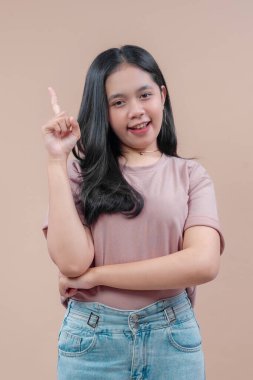 Uzun siyah saçlı, günlük tişört ve kot giyen Asyalı bir kadın, bir parmağını kaldırırken özgüvenle gülümsüyor, fikri, ilhamı ve pozitif ifadeyi sembolize ediyor..
