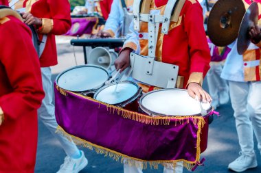 Kırmızı ve altın rengi üniformalı bir bando davulcusunun yakın çekimi. Geçit töreninde çoklu davul çalıyor. Ritmi, takım çalışmasını, kültürünü ve şenlikli kutlamaları gösteriyor..