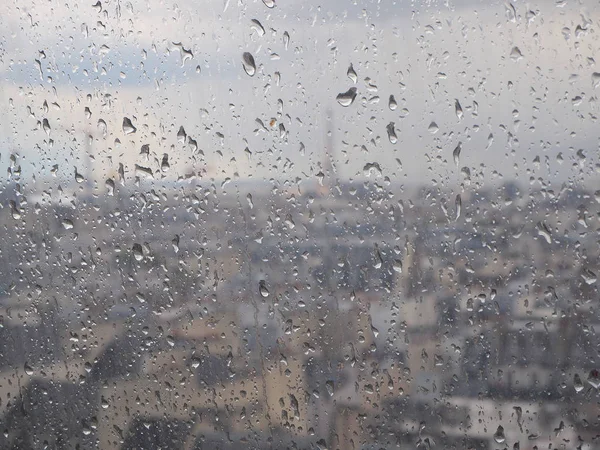 Glass with raindrops, blurred urban background, Paris, France