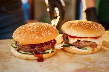 İki burger bir ahşap tahta üzerinde bitmiş. Açık mutfak sokakta. Sokak lokanta