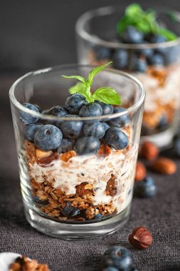 Ev yapımı granola kahvaltı yaban mersini ve yoğurt, gri bir arka plan üzerinde bardaklarda servis