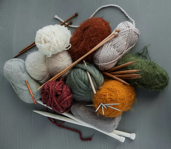 Knitting yarns, hooks and knitting needles on grey background.