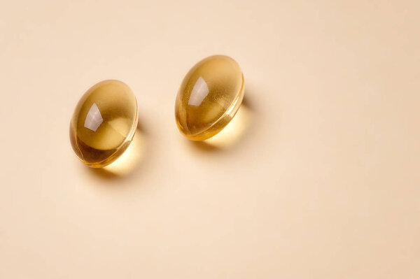 Желтые прозрачные таблетки рыбьего жира на бежевом фоне
