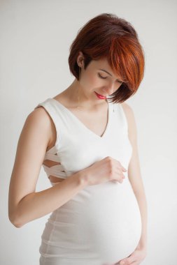 Işık arka plan üzerinde beyaz elbiseli genç hamile kadın