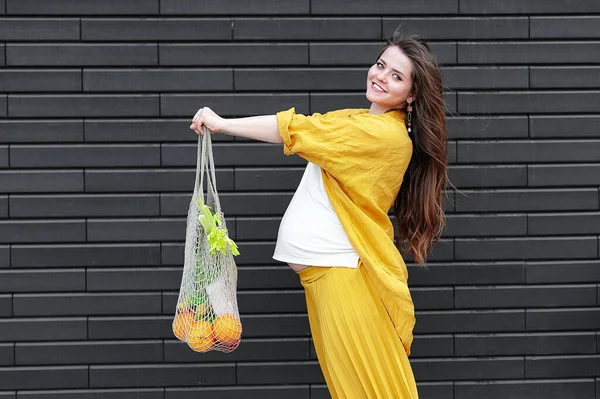 Siyah Duvarda Meyve Sebzelerle Dolu Sarı Elbiseli Hamile Bir Kadın — Stok fotoğraf
