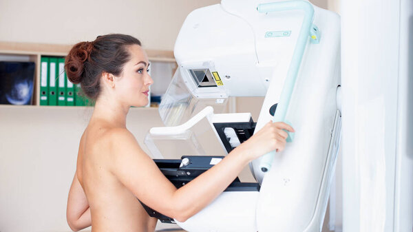 Young woman at breast cancer prevention screening at hospital. Hardware examination of the breast. Healthy young woman doing cancer prophylactic mammography scan. Modern hospital with hi-tech machine