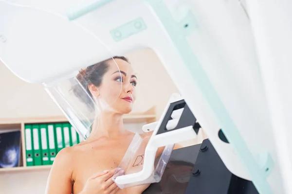 Young woman at breast cancer prevention screening at hospital. Hardware examination of the breast. Healthy young woman doing cancer prophylactic mammography scan. Modern hospital with hi-tech machine