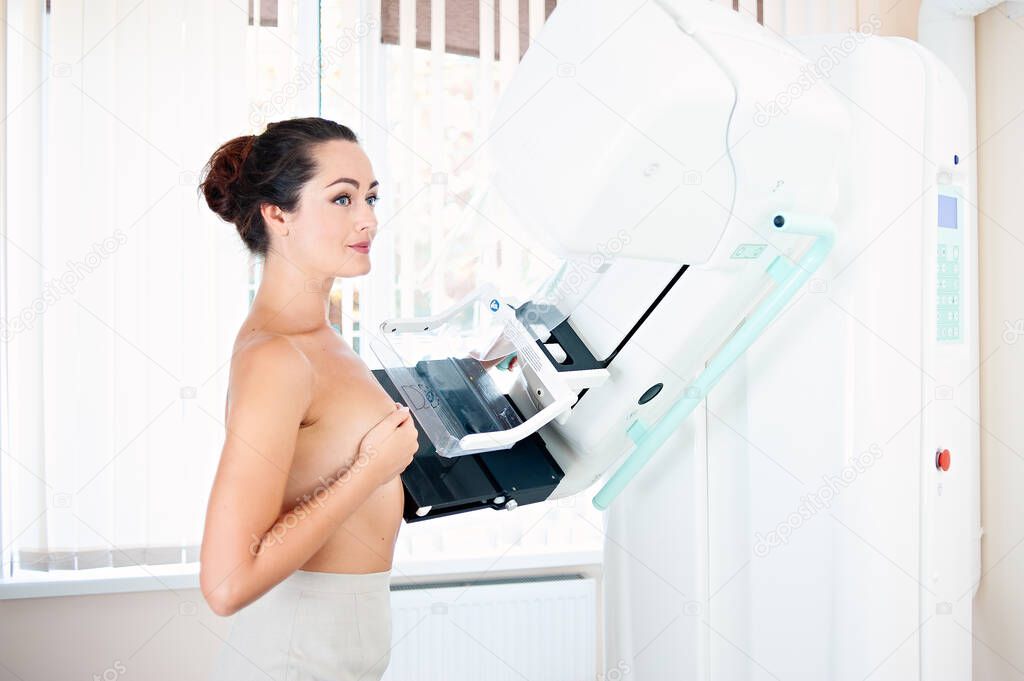 Young woman at breast cancer prevention screening at hospital. Hardware examination of the breast. Healthy young woman doing cancer prophylactic mammography scan. Modern hospital with hi-tech machine
