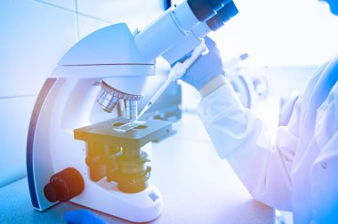 Bir laboratuvar çalışanı virüsleri mikroskopla inceler.