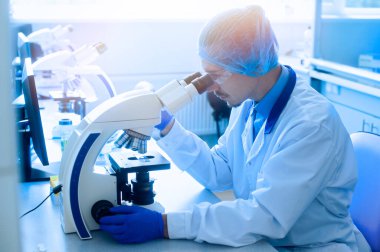 Bir laboratuvar çalışanı virüsleri mikroskopla inceler.