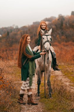 Genç bir kadın ve kızıl saçlı bir kız sonbaharda şaraphanede yürür ve atlara binerler. Boho tarzı