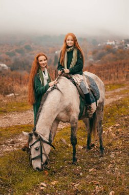 Genç bir kadın ve kızıl saçlı bir kız sonbaharda şaraphanede yürür ve atlara binerler. Boho tarzı