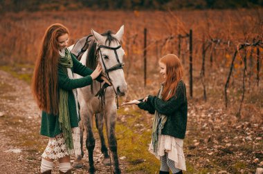 Genç bir kadın ve kızıl saçlı bir kız sonbaharda şaraphanede yürür ve atlara binerler. Boho tarzı