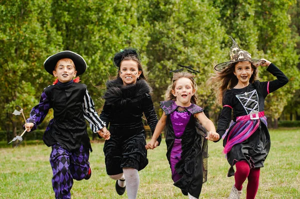 Cadılar Bayramı kostümlü mutlu çocuklar çimlerde koşuyor.