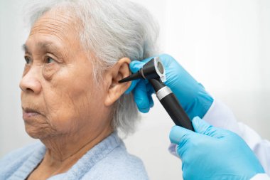 Otolaryngologist ya da ENT hekim doktoru yaşlı hasta kulağını otoskopla muayene ediyor, işitme sorunu var..