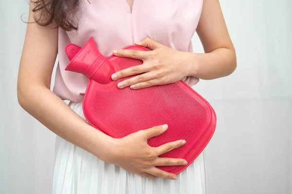 Karın ağrısını hafifletmek için sıcak su torbası kullanan bir kadın..