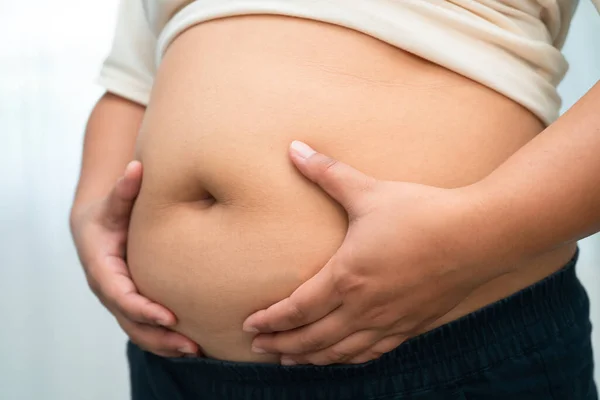 Asyalı kadın şişman göbeğini sıkmak için elini kullanıyor. Büyük boy aşırı kilolu ve obez..