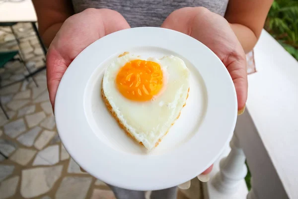 woman hand holding fried eggs in ideal heart on the white plate