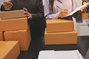 Küçük işletmeler kurma portresi KOBİ sahipleri ve iki Asyalı kadın online siparişleri kontrol ediyor. Ev işlerinde çalışan kutucuklarla çalışan ürünleri satıyorlar.