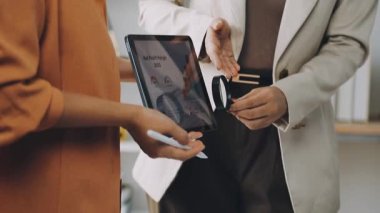 close up shot of young woman holding digital tablet and checking the details of her female colleague in office.