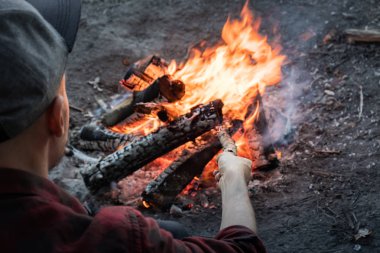 Kamp ateşi bir orman, yapma. Erkek kişi rahat kıyafetler içinde ahşap parçaları içine yanan ateşi koyar.