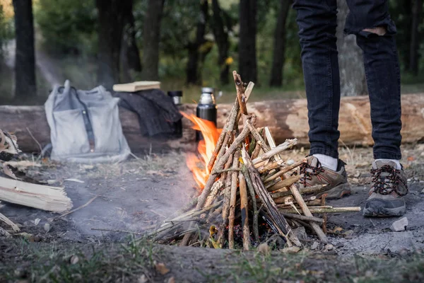 Kamp ateşi bir orman yanıyor. Vahşi kavramı içine seyahat: vintage sırt çantası, termos ve açık havada bir şömine yakınındaki trekking Ayakkabı Erkek ayak kamp yeri