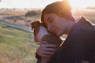 Bir köpek güzel doğada günbatımında sarılma. Akşam güneşin bakan kadın ile onun evde beslenen hayvan yanında oturur