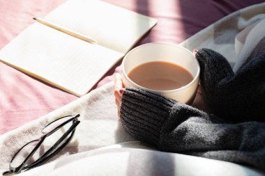 Kahve içer ve tembel güneşli sabahı yatakta okuma. Erkek dumanı tüten yatakta okuma sıcak kakao fincan tutan eller