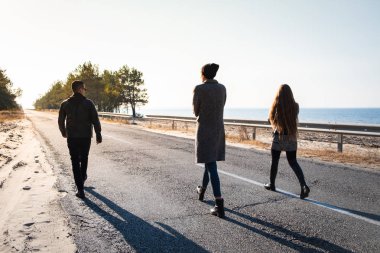 İnsanlar yürüyüş deniz kenarında yol boyunca grup. Üç genç kişi yaz sonu veya sonbaharda güzel doğa sahnede yürümek