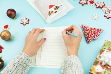 Yazma Noel tebrik mektubu. Kalem ile eller üstten görünüm kağıt, tatil sahne ve hediyeler ve yeni yıl kartı ile mavi arka plan üzerinde