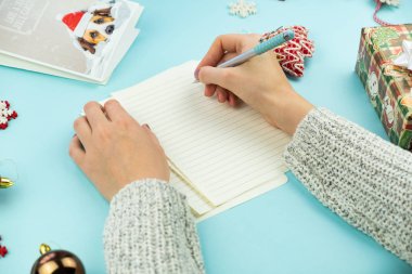 Yazma Noel tebrik mektubu. Kalem ile eller üstten görünüm kağıt, tatil sahne ve hediyeler ve yeni yıl kartı ile mavi arka plan üzerinde